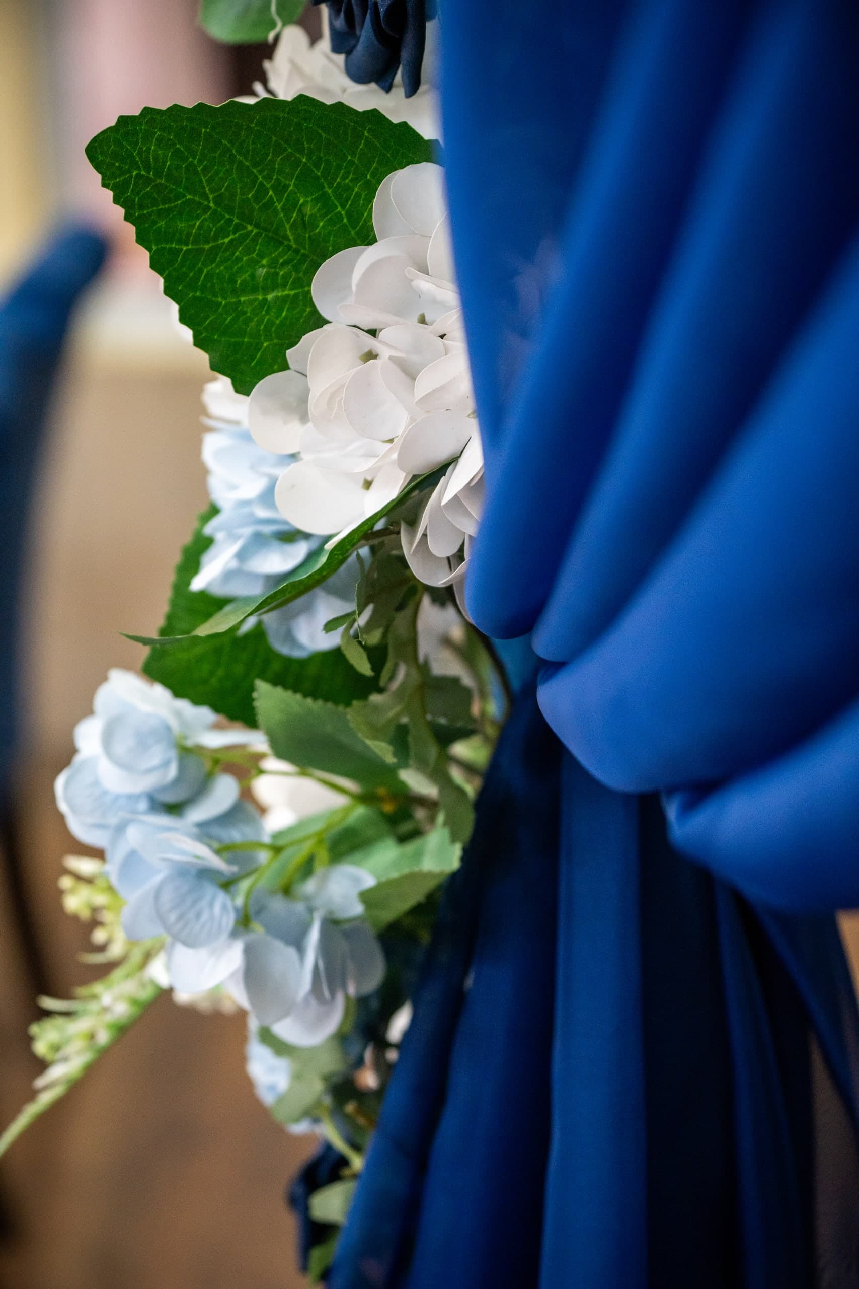 Close view of white and pale blue artificial hydrangeas beside folds of royal blue drapery.
