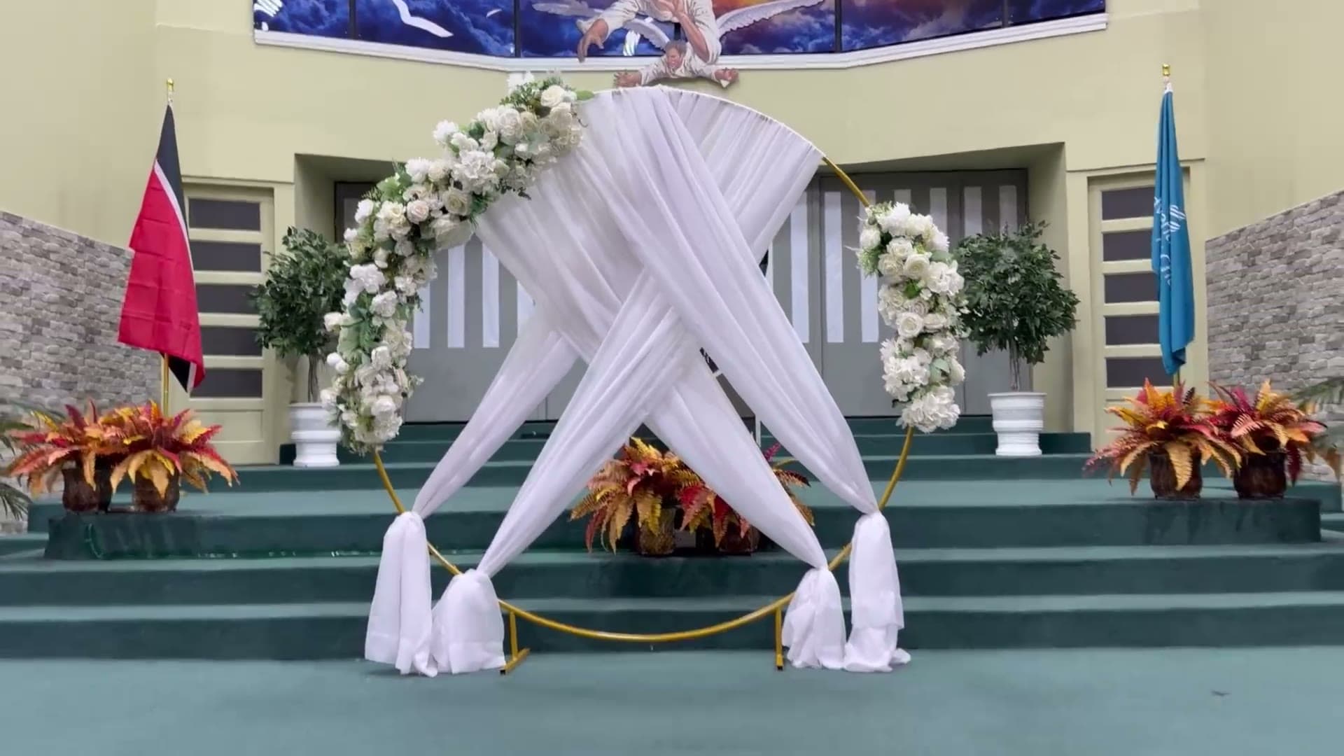 A church sanctuary with a white draped floral arch at the altar and white pew bows tied with emerald ribbon.